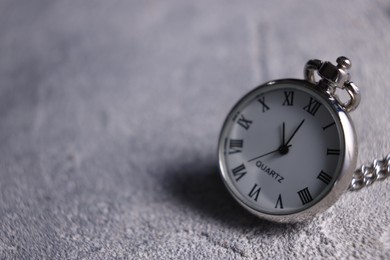 Silver pocket clock on grey textured table, closeup. Space for text