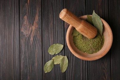 Photo of Mortar with whole and ground aromatic bay leaves on wooden table, flat lay. Space for text