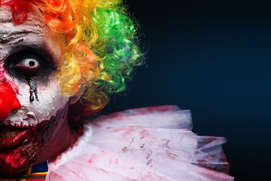 Photo of Terrifying clown on dark background, closeup. Halloween party costume