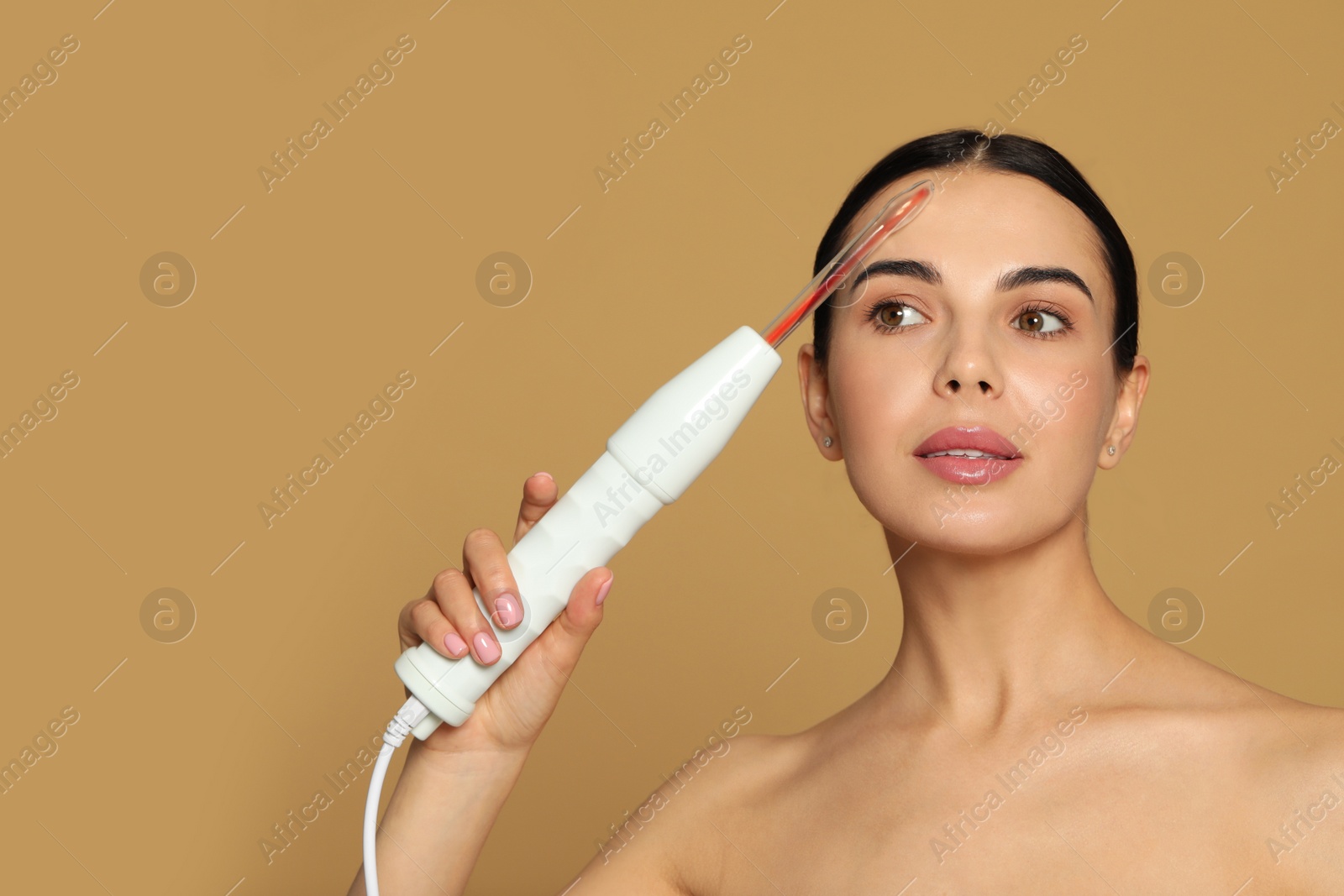 Photo of Woman using high frequency darsonval device on beige background. Space for text