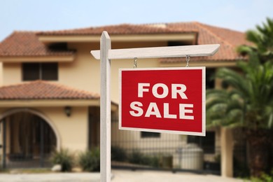 Sale sign near beautiful house outdoors. Red signboard with words