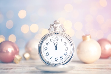 Photo of Pocket watch and festive decor on table against blurred lights. New Year countdown