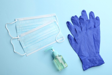 Photo of Medical gloves, masks and hand sanitizer on light blue background, flat lay