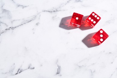 Photo of Three red game dices on white marble table, flat lay. Space for text