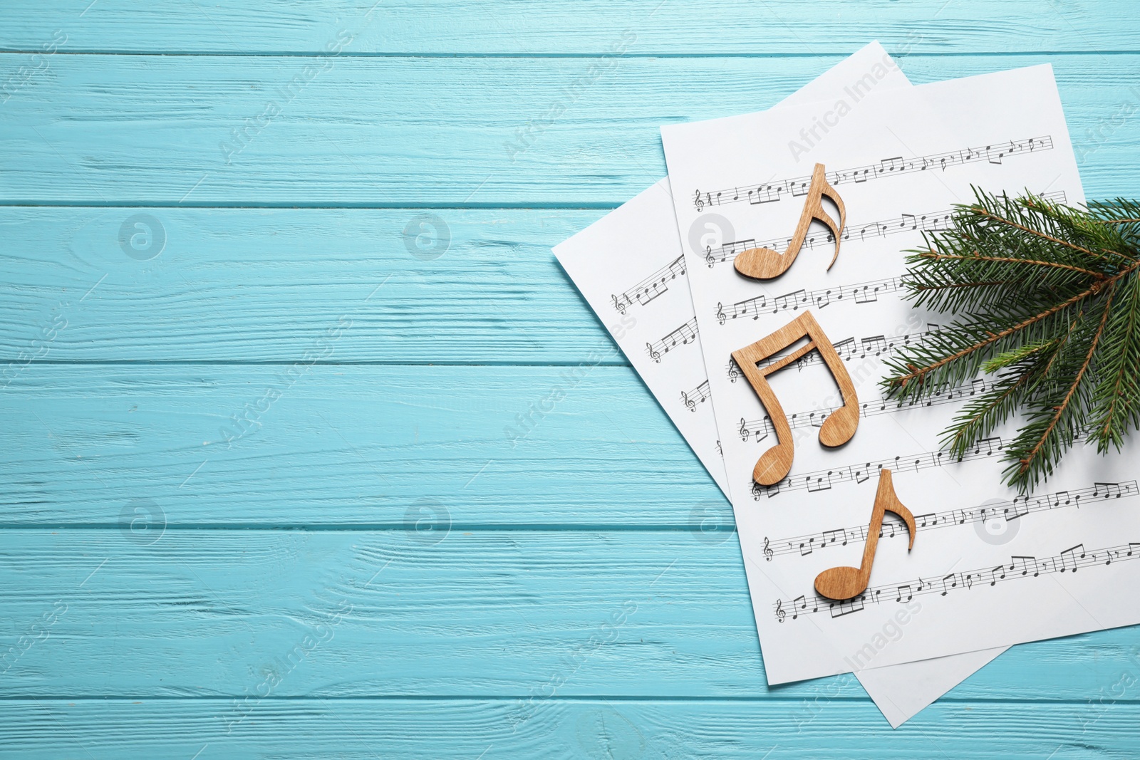 Photo of Christmas tree branch, notes and music sheets on blue wooden table, flat lay with space for text
