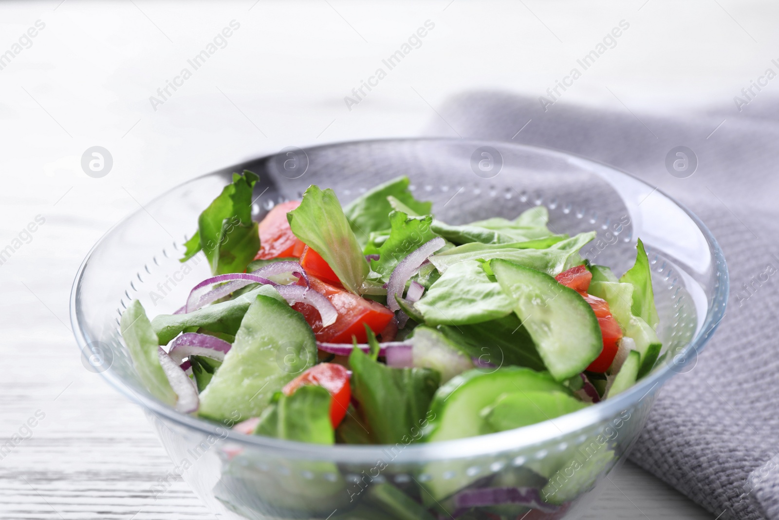 Photo of Bowl of tasty salad with cucumber, tomato and lettuce on table