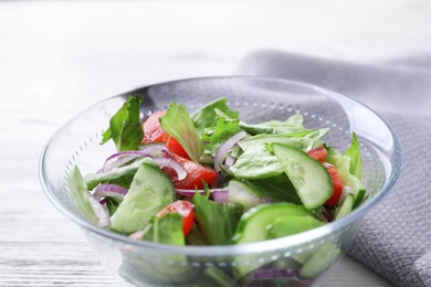 Photo of Bowl of tasty salad with cucumber, tomato and lettuce on table