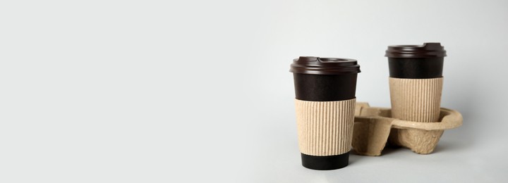 Image of Takeaway paper coffee cups with sleeves, plastic lids and cardboard holder on light grey background, space for text. Banner design