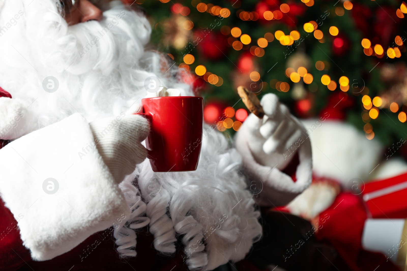 Photo of Santa Claus with hot drink and cookie against blurred Christmas lights, closeup