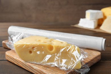 Photo of Block of cheese with plastic food wrap on wooden table. Space for text