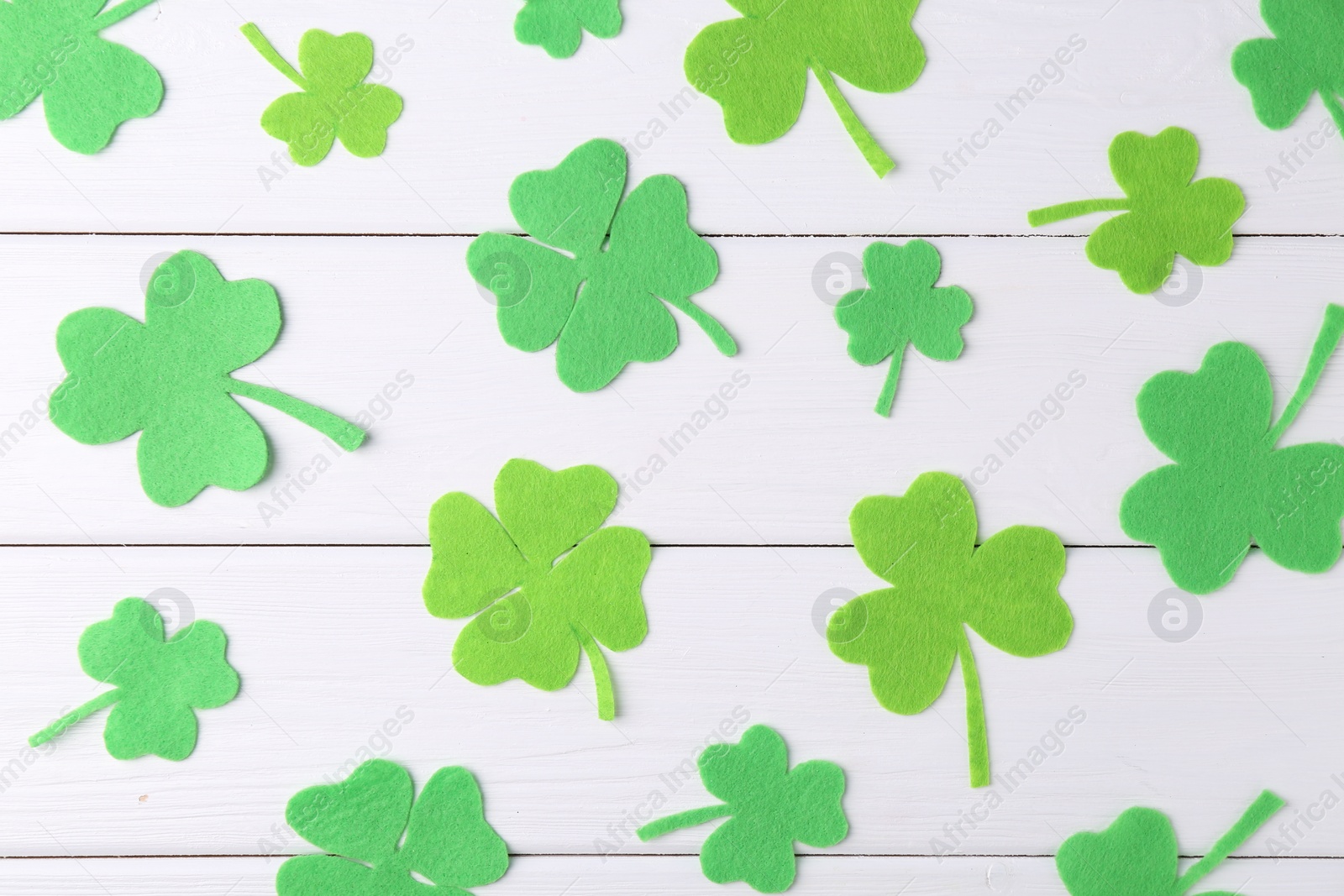 Photo of St. Patrick's day. Decorative green clover leaves on white wooden table, flat lay