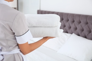 Photo of Young chambermaid with clean towels in bedroom, closeup. Space for text