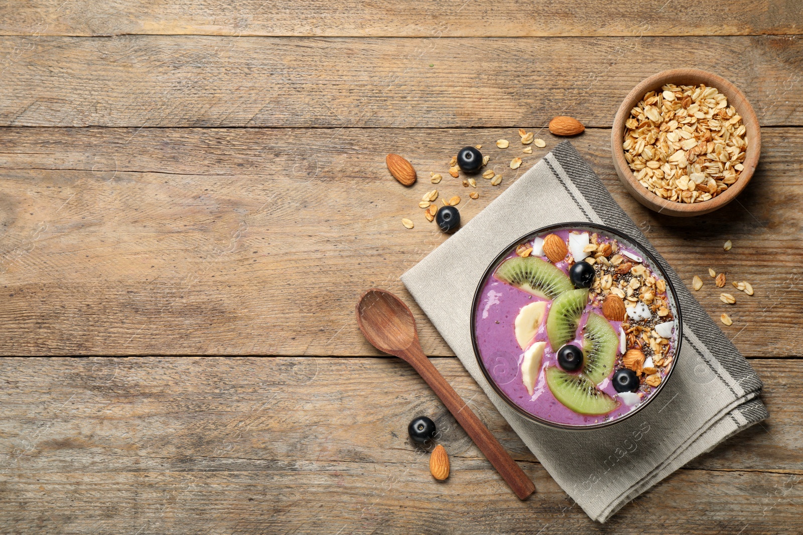 Photo of Delicious acai smoothie with granola and fruits served on wooden table, flat lay. Space for text