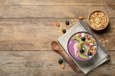 Delicious acai smoothie with granola and fruits served on wooden table, flat lay. Space for text