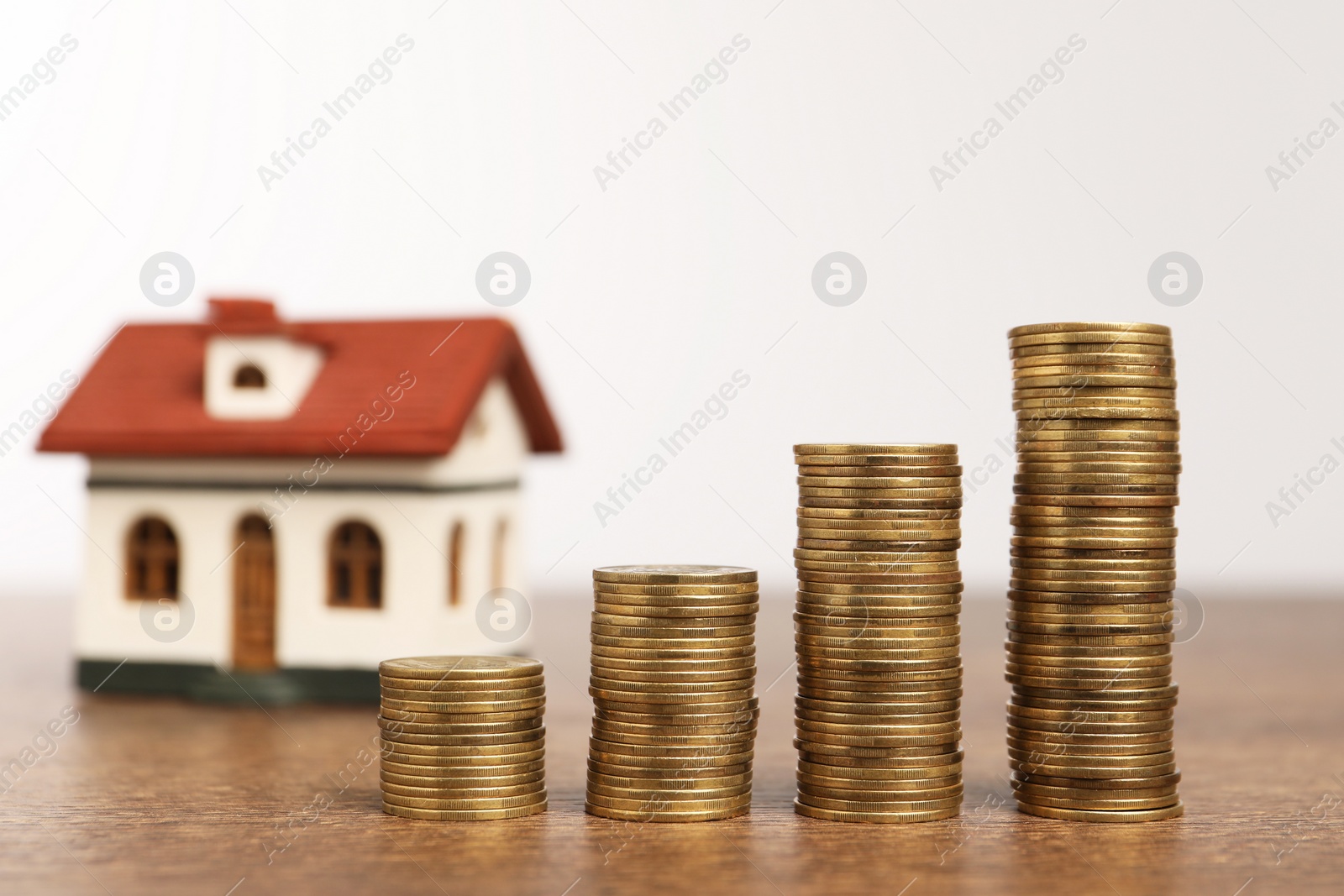 Photo of Mortgage concept. House model and stacks of coins on wooden table against white background, selective focus