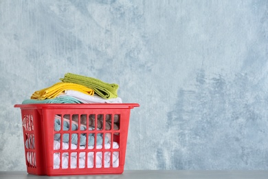 Photo of Basket with clean laundry on table against color background, space for text
