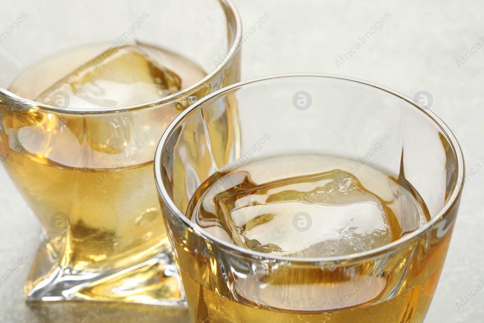 Photo of Tasty whiskey with ice in glasses on light table, closeup