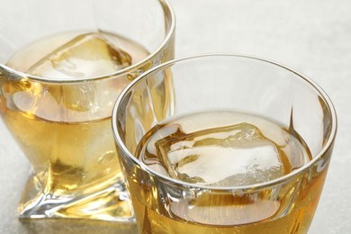 Photo of Tasty whiskey with ice in glasses on light table, closeup