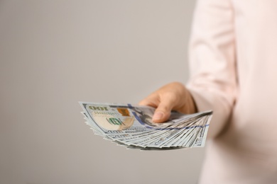 Photo of Young woman holding dollar bills on light grey background, closeup