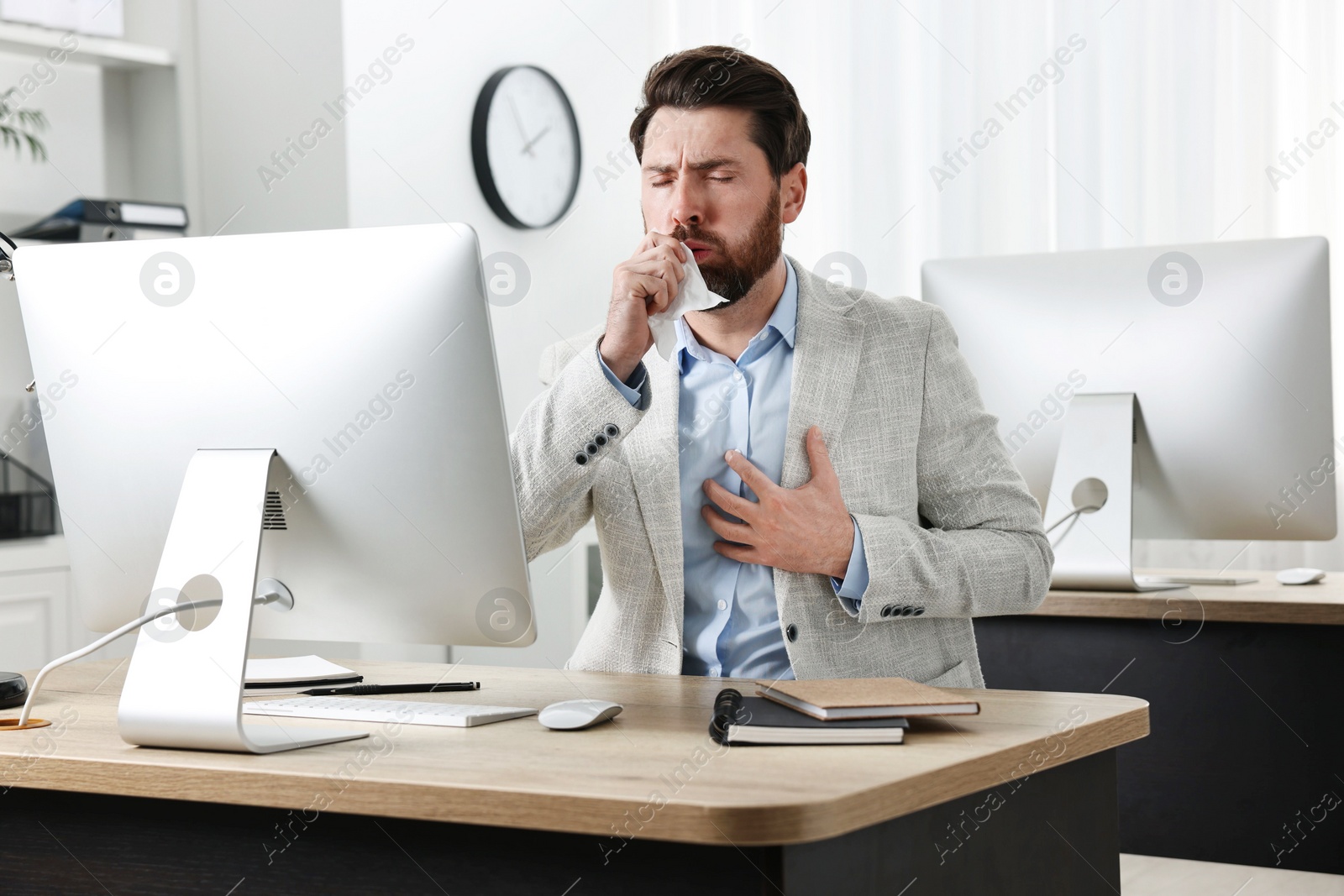 Photo of Sick man with tissue coughing at workplace in office