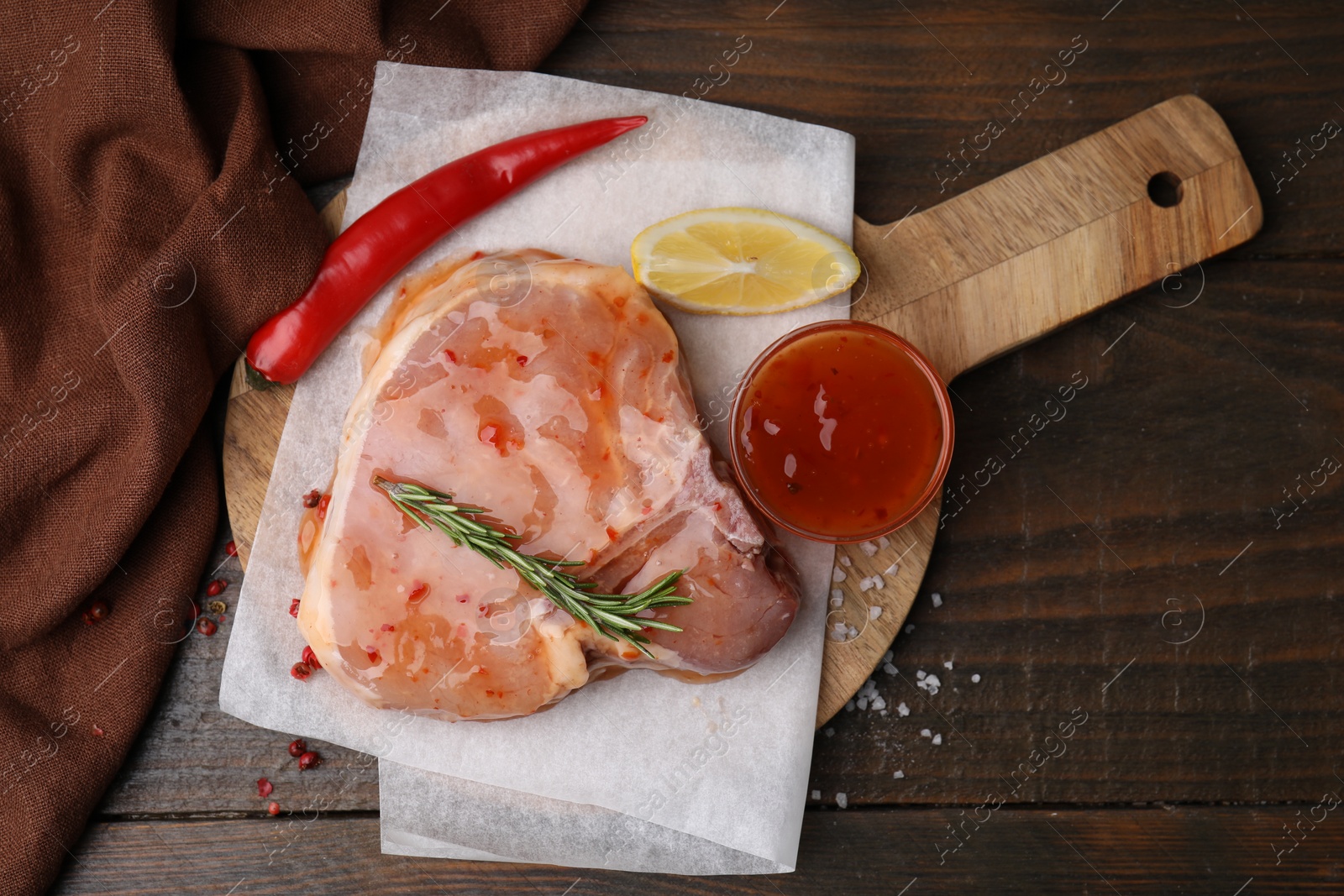 Photo of Board with raw marinated meat, lemon, rosemary and spices on wooden table, top view