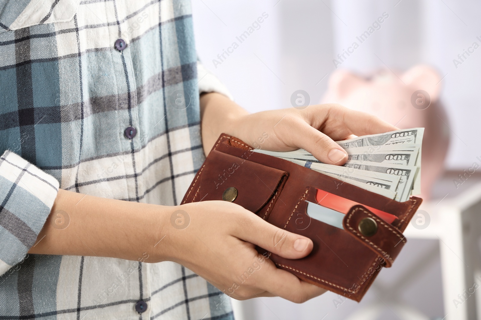 Photo of Woman putting money into wallet on blurred background, closeup