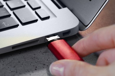Photo of Woman attaching usb flash drive into laptop at light grey table, closeup