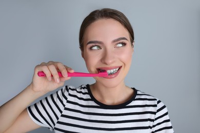 Photo of Young woman brushing teeth with charcoal toothpaste on grey background