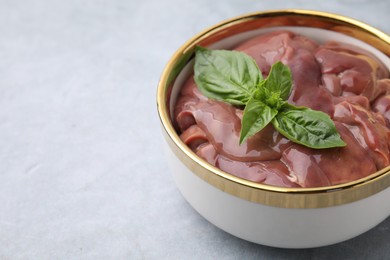 Photo of Bowl with raw chicken liver and basil on light grey table, closeup. Space for text