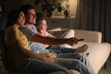 Family watching movie with popcorn on sofa at night