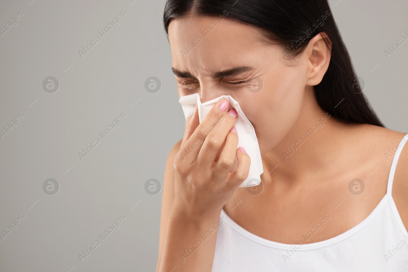 Photo of Suffering from allergy. Young woman blowing her nose in tissue on light grey background. Space for text