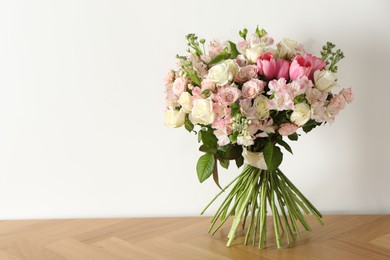 Photo of Beautiful bouquet of fresh flowers on wooden table near white wall, space for text