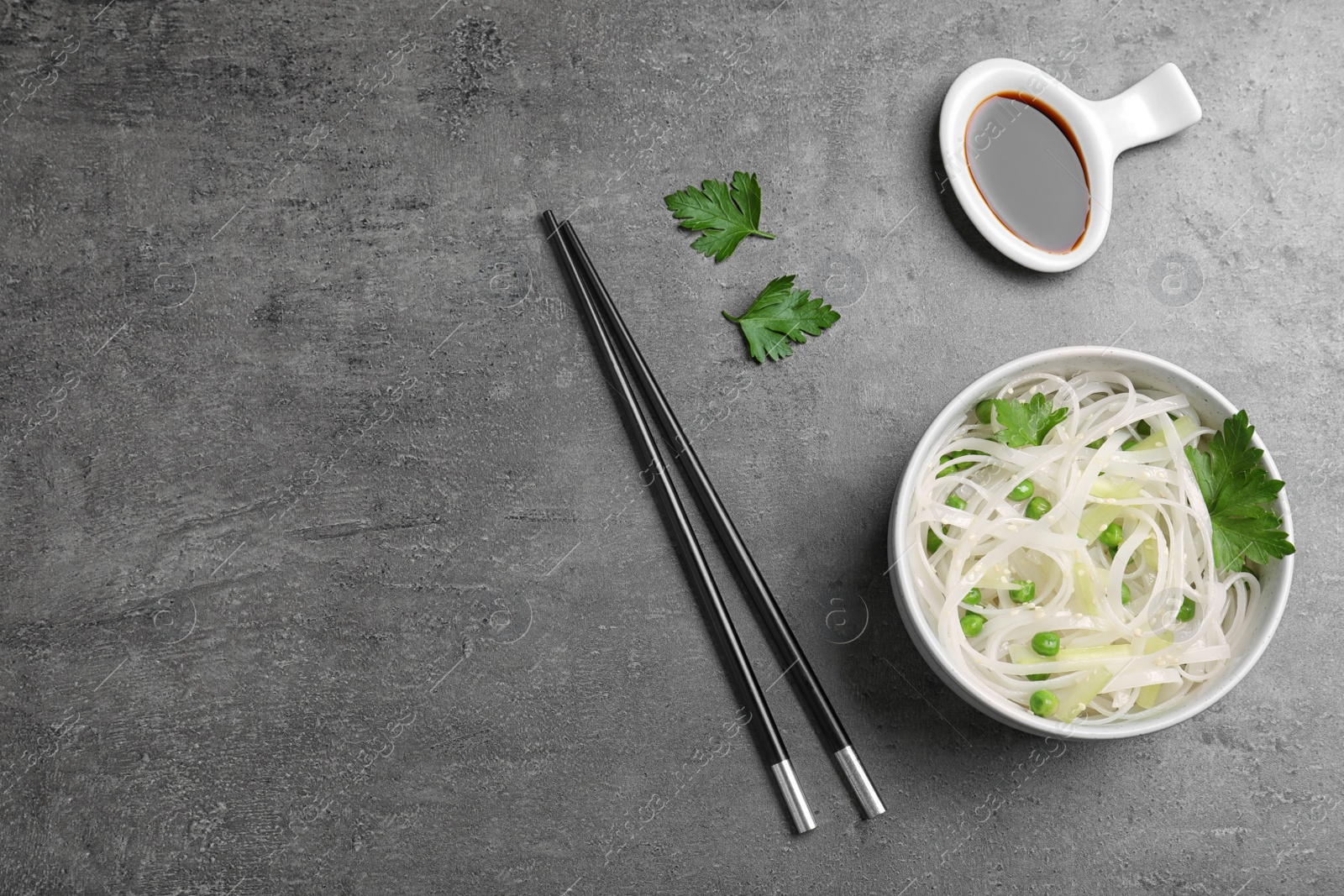 Photo of Bowl of rice noodles with chopsticks on grey background, flat lay. Space for text