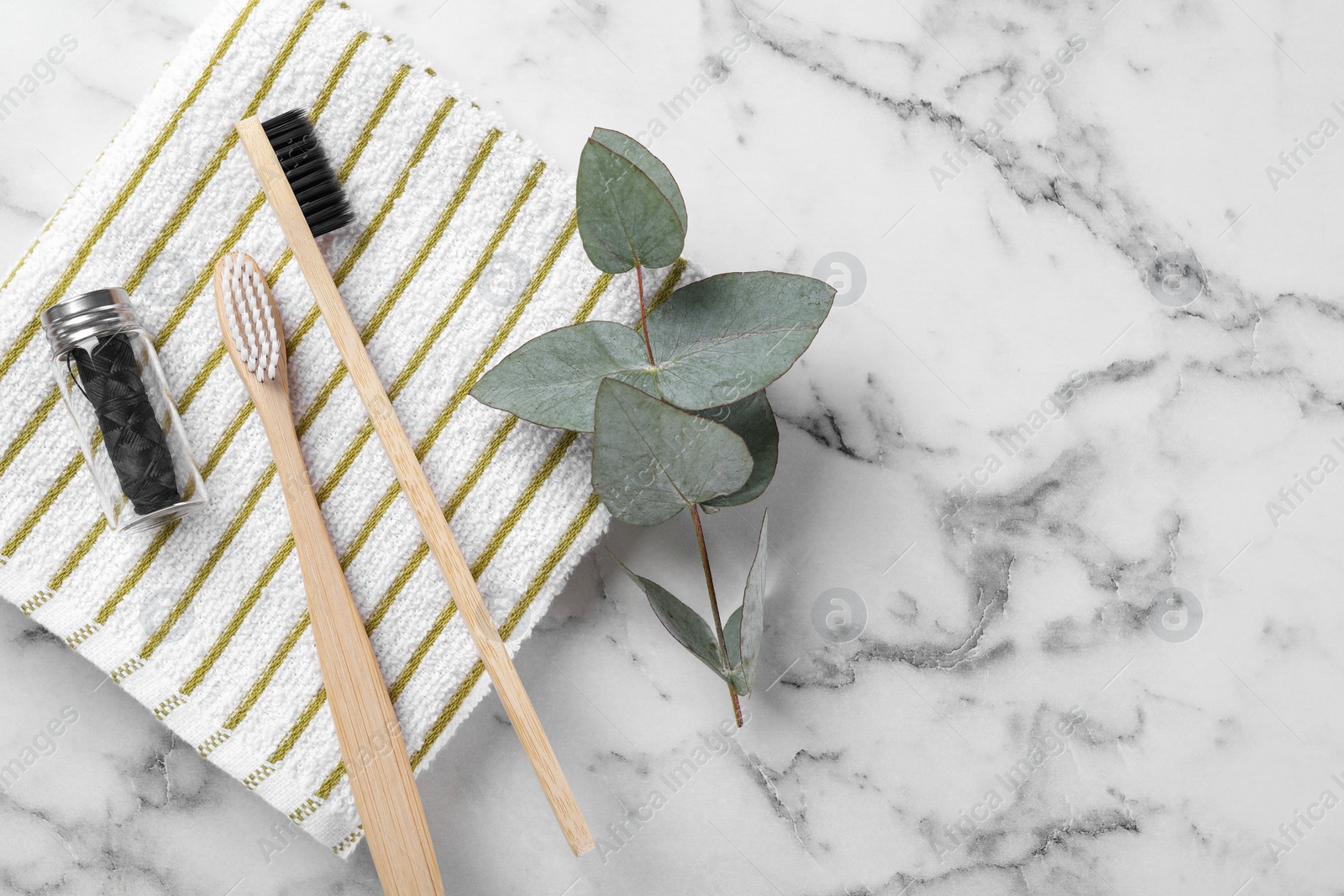 Photo of Bamboo toothbrushes, natural dental floss, towel and eucalyptus branch on white marble table, flat lay. Space for text