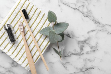 Bamboo toothbrushes, natural dental floss, towel and eucalyptus branch on white marble table, flat lay. Space for text