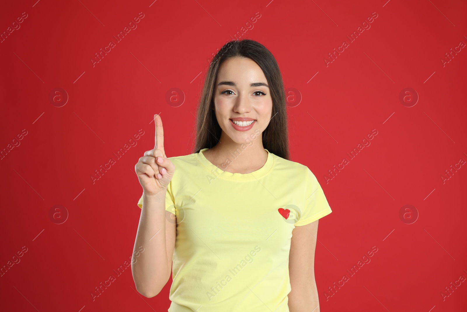 Photo of Woman in yellow t-shirt showing number one with her hand on red background