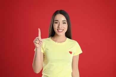 Woman in yellow t-shirt showing number one with her hand on red background