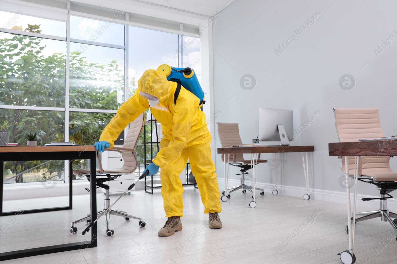 Photo of Janitor in protective suit disinfecting office to prevent spreading of COVID-19