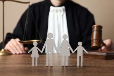 Photo of Family law. Judge with gavel and scales of justice sitting at wooden table, focus on figure of parents and children