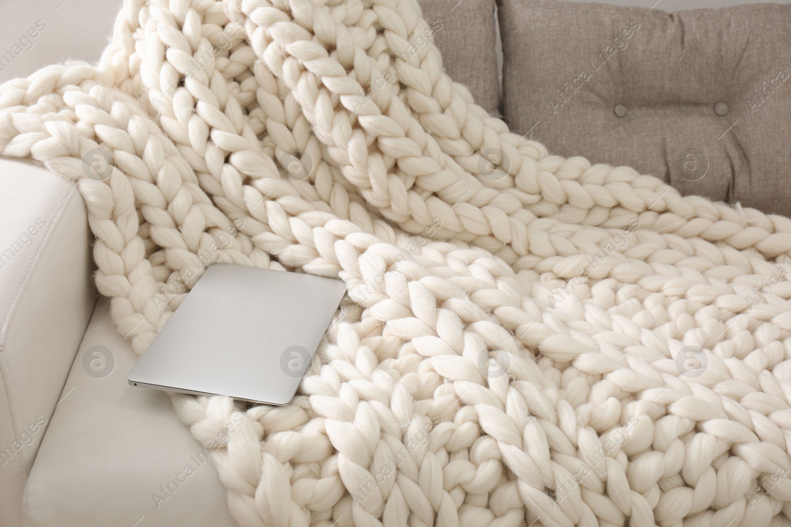 Photo of Soft knitted blanket and modern laptop on couch in room. Interior element