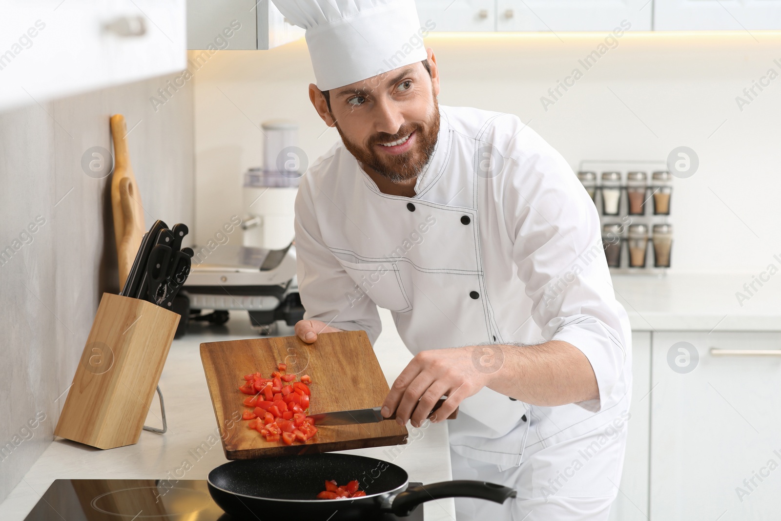 Photo of Happy chef putting cut tomatoes into frying pan indoors