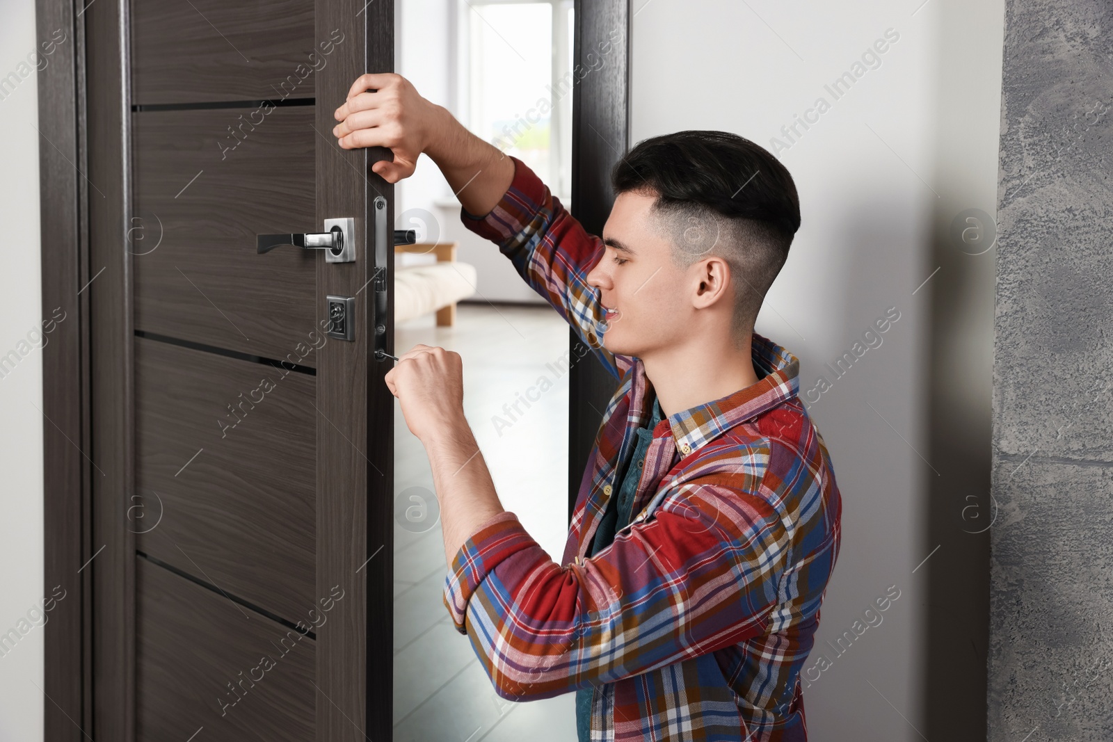 Photo of Young handyman repairing door lock in room