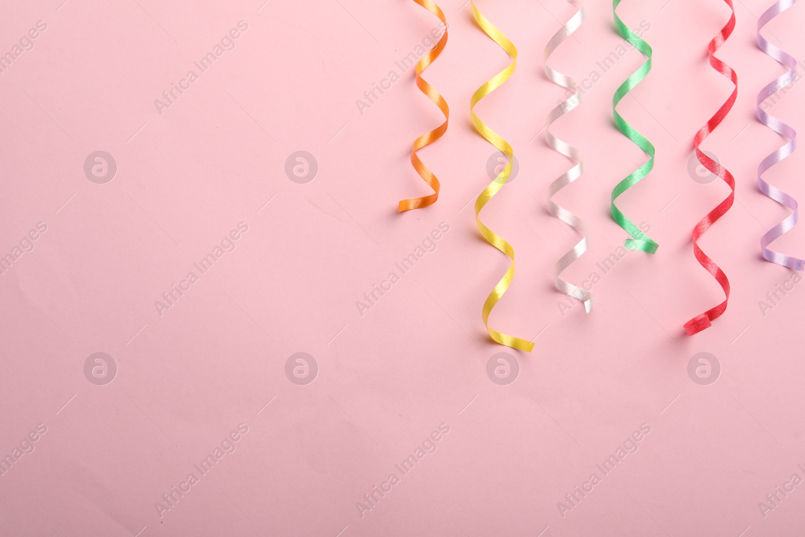 Photo of Colorful serpentine streamers on pink background, flat lay. Space for text