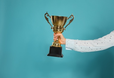 Photo of Young woman holding gold trophy cup on blue background, closeup