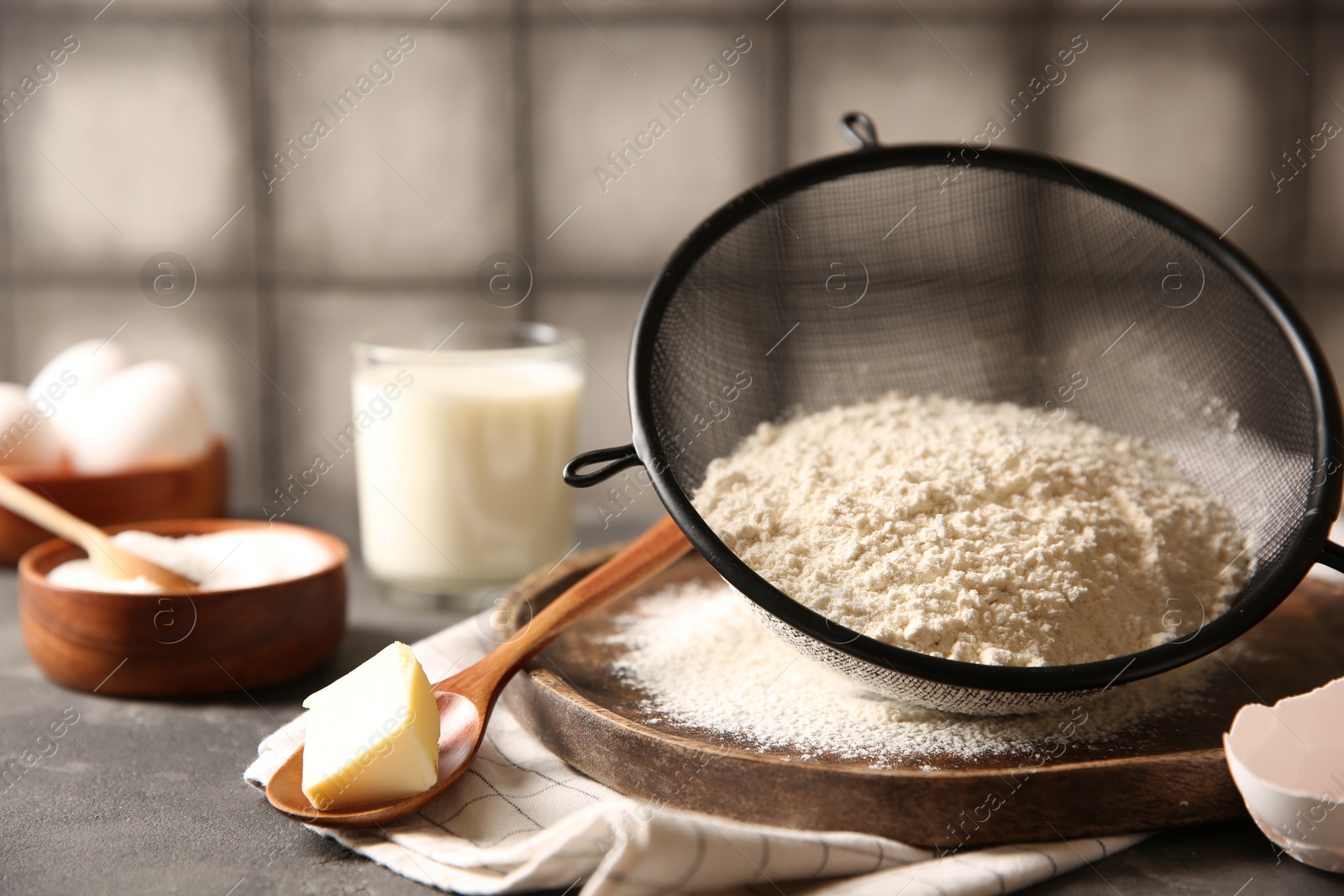 Photo of Making dough. Flour in sieve, spoon and butter on grey table, closeup