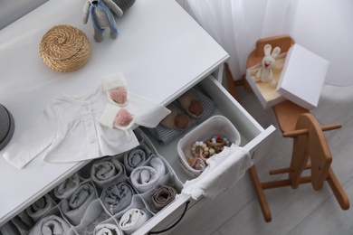 Photo of Modern open chest of drawers with baby clothes and accessories in room, above view