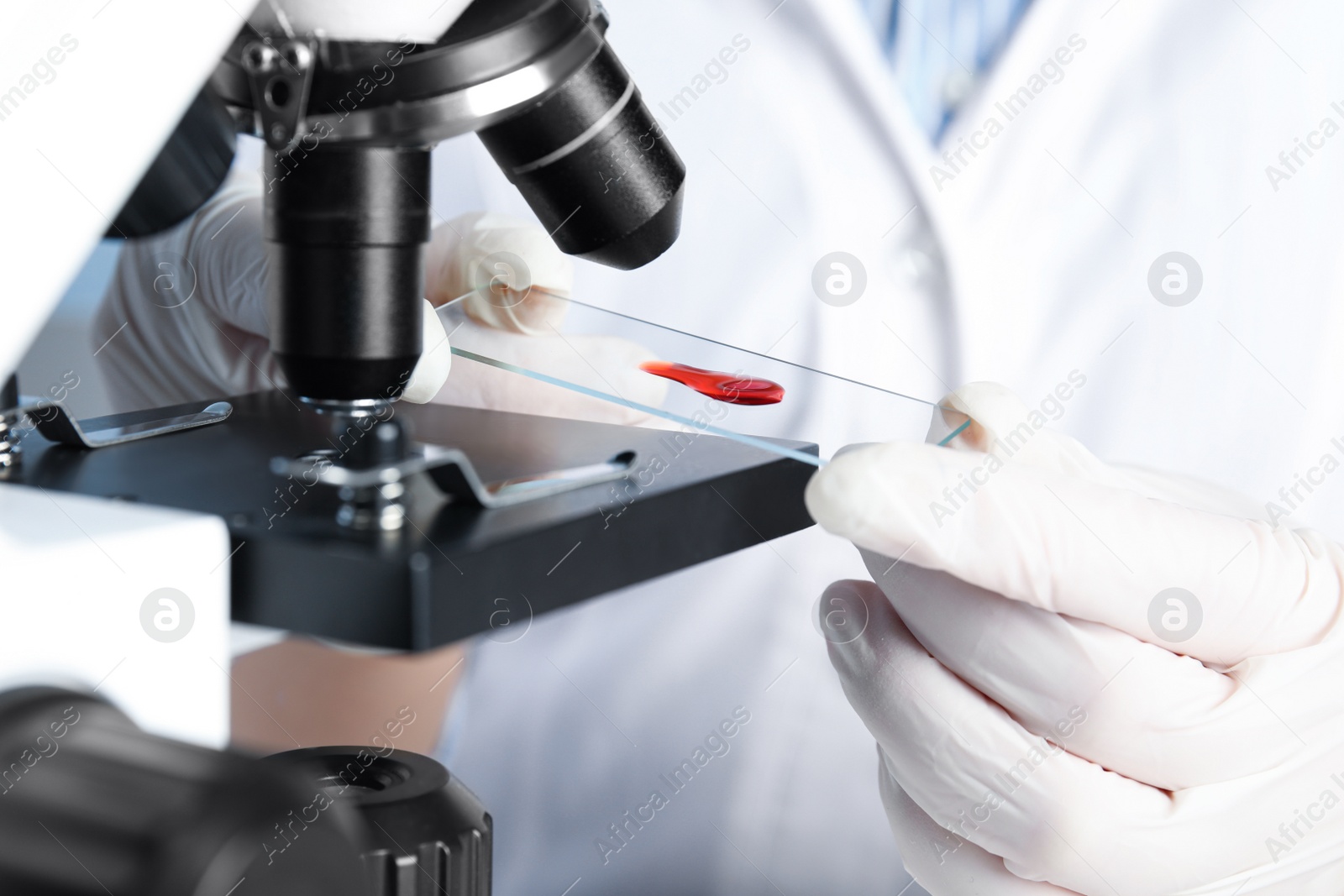 Photo of Scientist holding slide with blood sample near microscope in laboratory, closeup. Virus research