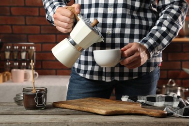 Photo of Man pouring aromatic coffee from moka pot into cup at table in kitchen, closeup