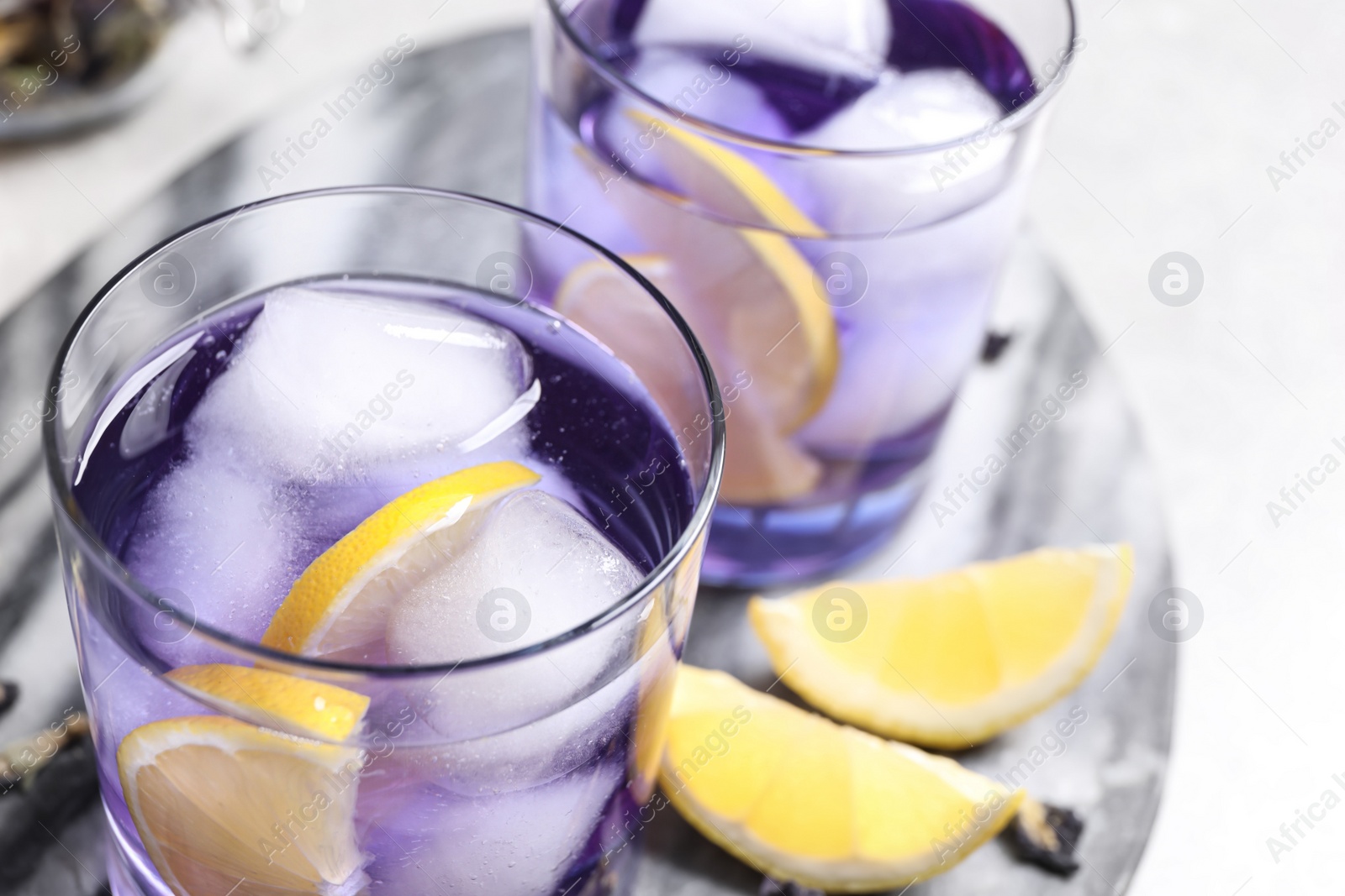 Photo of Organic blue Anchan with lemon and ice cubes on table, closeup. Herbal tea