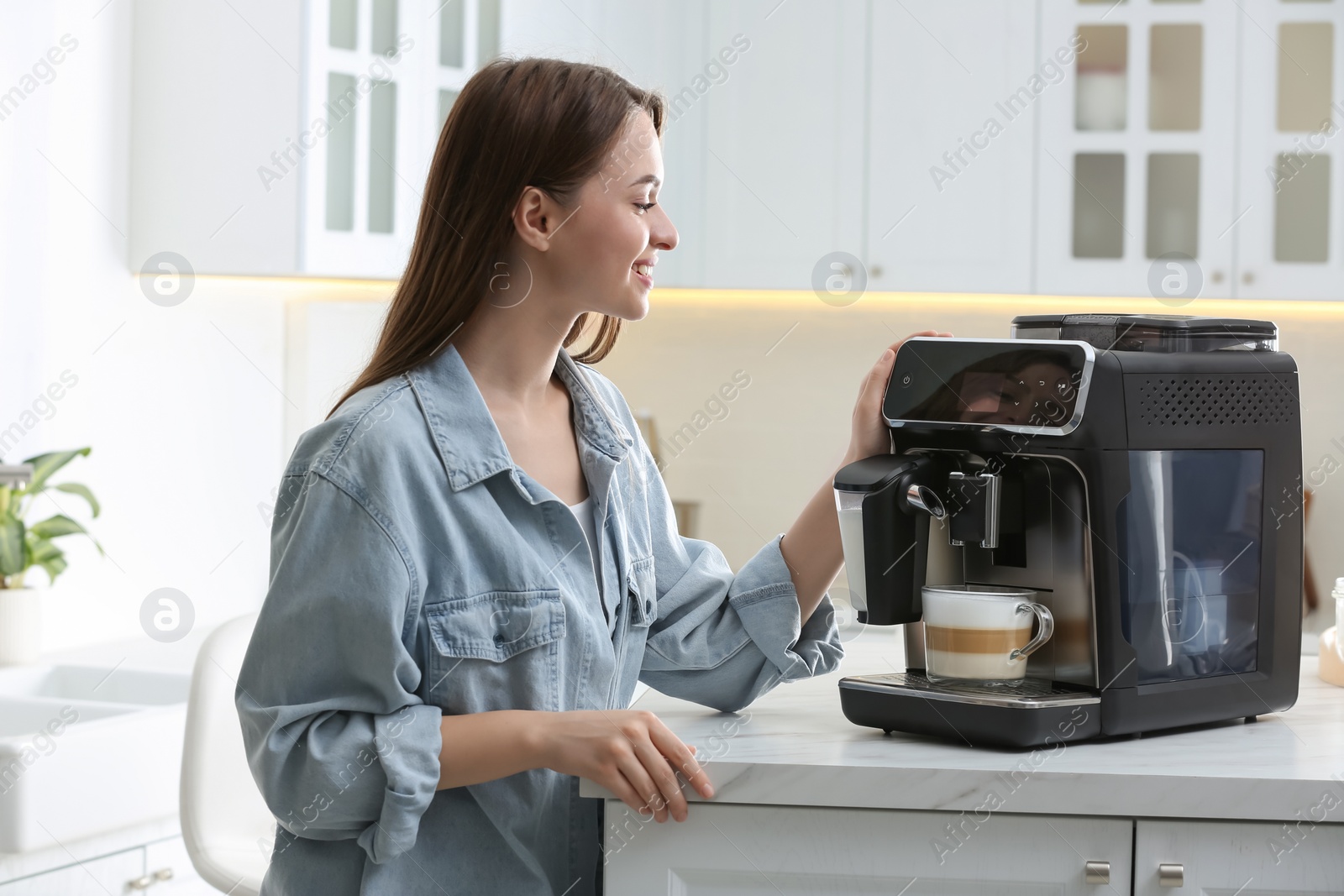 Photo of Young woman preparing fresh aromatic coffee with modern machine in kitchen